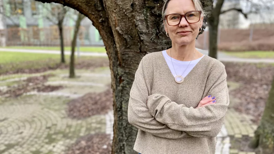 Porträtt av barnmorskan och forskaren Pernilla Ny, Hon står vid ett träd med armarna i kors. Hon har beige tröja och glasögon.