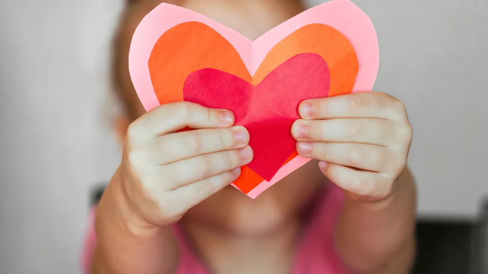 Barn håller utklippta hjärtan i röd, orange, rosa framför sig. Foto: iStock