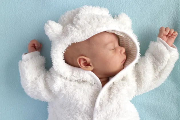Bebis i teddyoverall mot blå bakgrund, fotografi. Foto: iStock