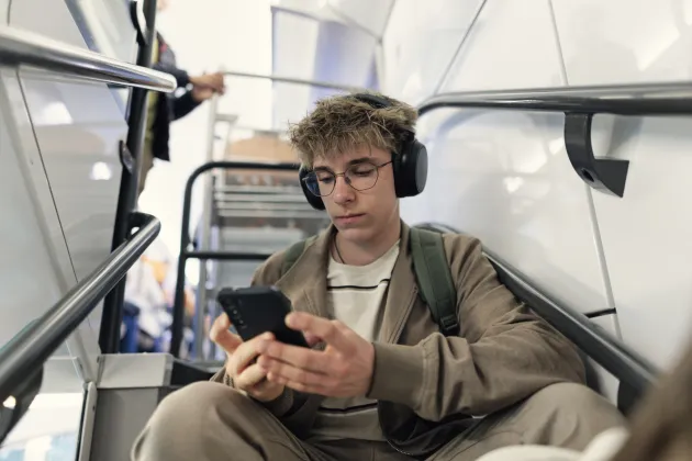 En ung man sitter och tittar på mobilen i ett tunnelbanetåg. Foto: iStock