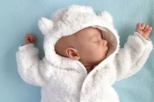 Bebis i teddyoverall mot blå bakgrund, fotografi. Foto: iStock