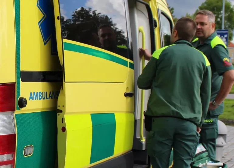 Två ambulansmedarbete vid sitt fordon. Foto.