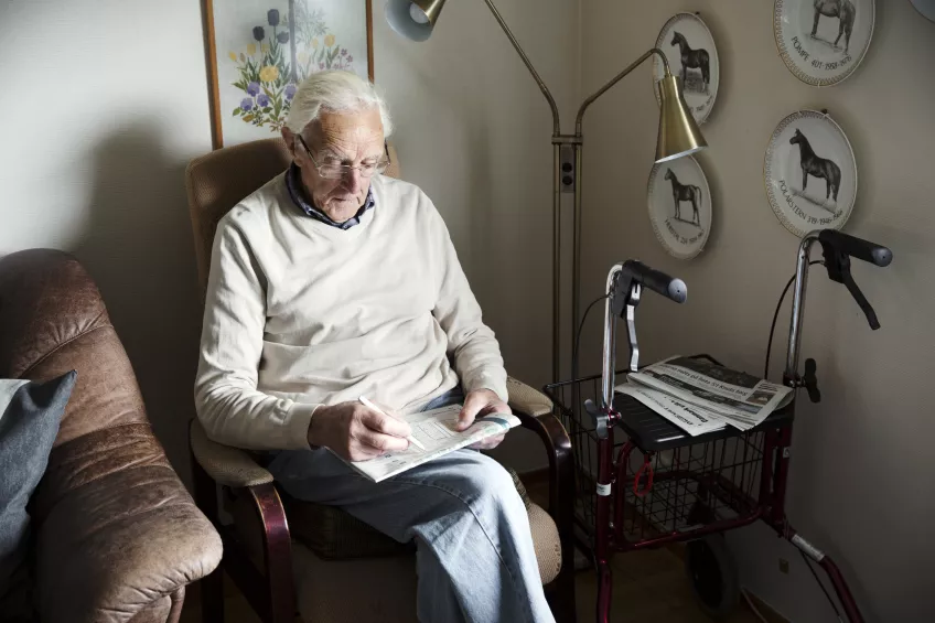 En äldre man sitter i en fåtölj i sitt hem. Foto.