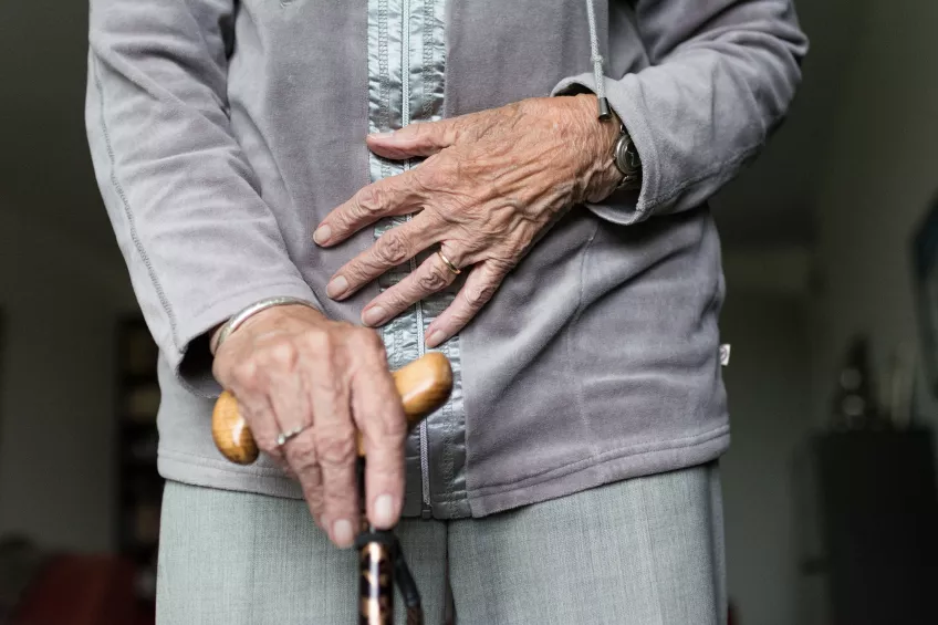 Del av kroppen på en äldre kvinna som håller i en käpp.