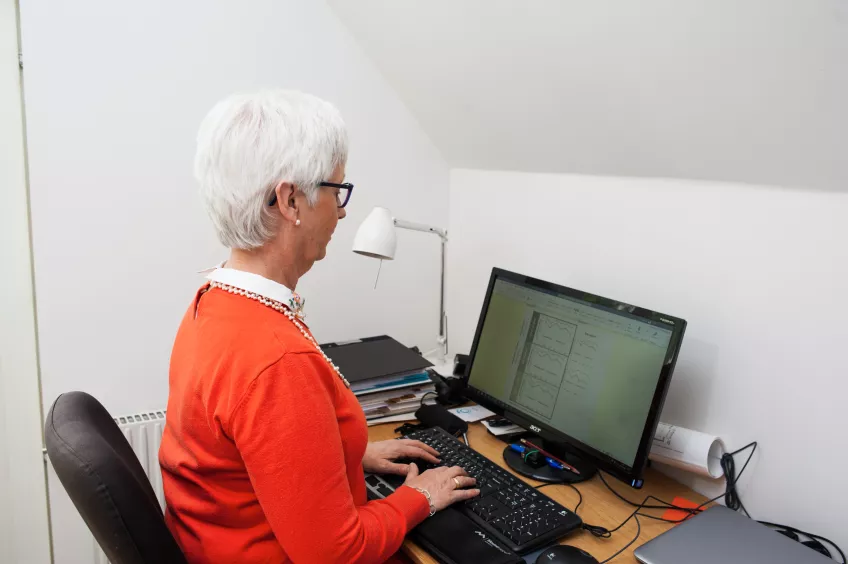 Eva Ekvall Hansson sitter vid ett skrivbord med en dator och jobbar.