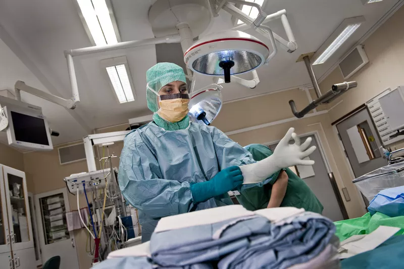 Medarbetare i vården tar på sig operationskläder. Foto.