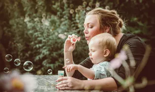 Kvinna och litet barn som blåser såpbubblor tillsammans. Foto.